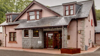A two-story veterinary hospital with slate roof and large windows, surrounded by trees. Sign reads,  A two-story veterinary hospital with slate roof and large windows, surrounded by trees. Sign reads,