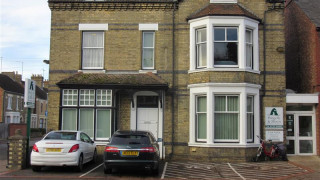 A two-story brick building with two cars parked in front, featuring a sign that reads  A two-story brick building with two cars parked in front, featuring a sign that reads