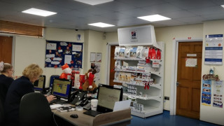 People work at computer stations in an office decorated for Christmas. On the right, shelves display pet products, and posters with announcements cover the walls. Text includes:  People work at computer stations in an office decorated for Christmas. On the right, shelves display pet products, and posters with announcements cover the walls. Text includes:
