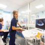 Vets Now Glasgow ICU Ultrasound machine displays an image while a medical professional examines equipment beside a patient bed. Another professional takes notes. The room is brightly lit with a wall clock showing 12:36.