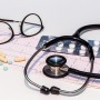 Vets-Now-dangers-ibuprofen-paracetamol-dogs-pets A stethoscope rests on an electrocardiogram, surrounded by scattered pills, eyeglasses, and a blister pack of tablets, creating a medical-themed setting.