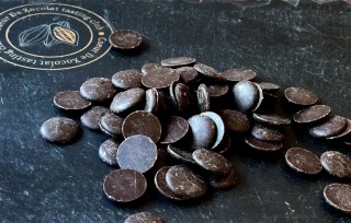 Chocolate discs lie scattered on a dark surface, near a circular logo with 