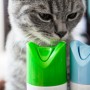 Cat poisoning dangers A gray tabby cat sniffs two air freshener cans, one green and one blue, positioned closely together on a table in an indoor setting.
