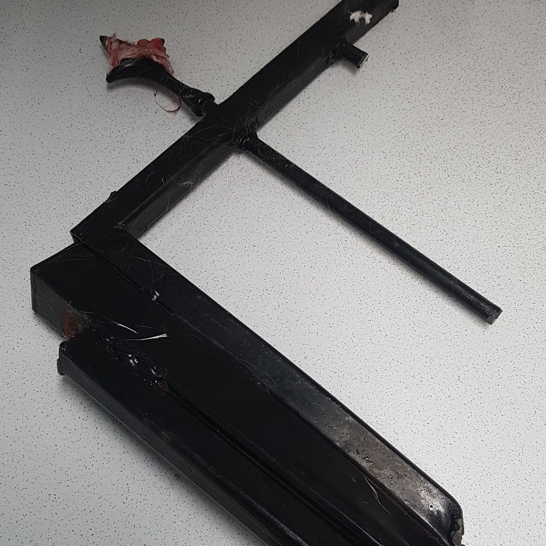 A black metal frame with sharp edges is lying on a speckled white surface, with some red fabric tangled on one end.