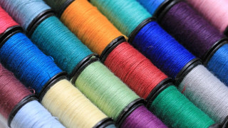 Spools of multicolored thread neatly arranged in parallel rows, showcasing vibrant blues, reds, greens, and purples on a smooth, reflective surface.