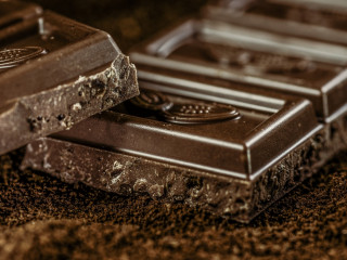 A close-up of two pieces of dark chocolate resting on each other, with rough edges against a textured brown surface.