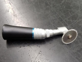 A handheld glass cutter with a black handle and silver cutting wheel is placed on a dark, scratched surface.