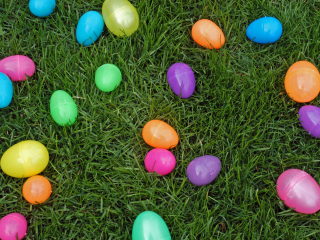 Colorful plastic eggs scattered on green grass, suggesting an Easter egg hunt setting with vibrant, festive decorations.