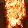 dog costume fire hazard warning Flames engulf a wooden object in a controlled burn, producing intense fire and smoke against a dark, indoor background.