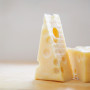 cheese 2-min A wedge of Swiss cheese, showcasing multiple holes, rests on a light wooden surface with soft, natural lighting in the background.