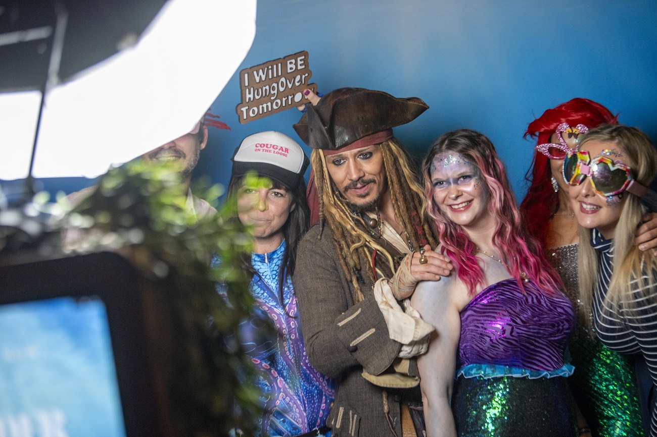 Group of colleagues in fancy dress posing for a photobooth with playful expressions and props during a Vets Now party.