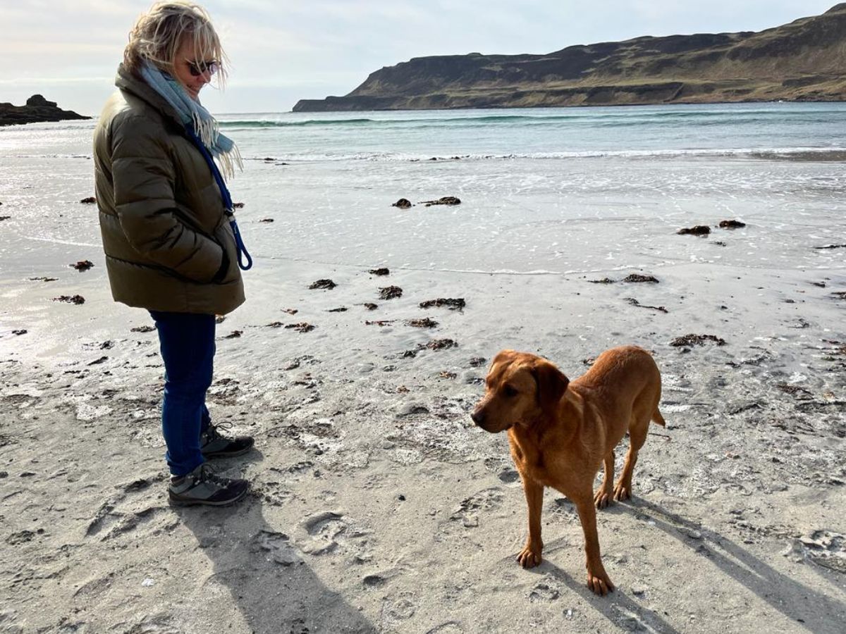 Woman walking with her Labrador named Nala along a wintry beach with cliffs in the background
