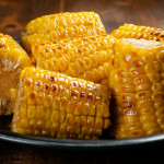 A tray of various pieces of grilled corn on the cob