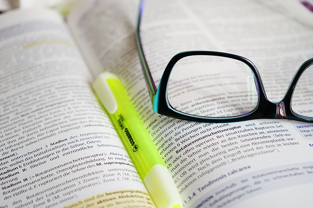 A pair of black-framed glasses rests on an open book with text, accompanied by a yellow highlighter, suggesting a study or reading session.