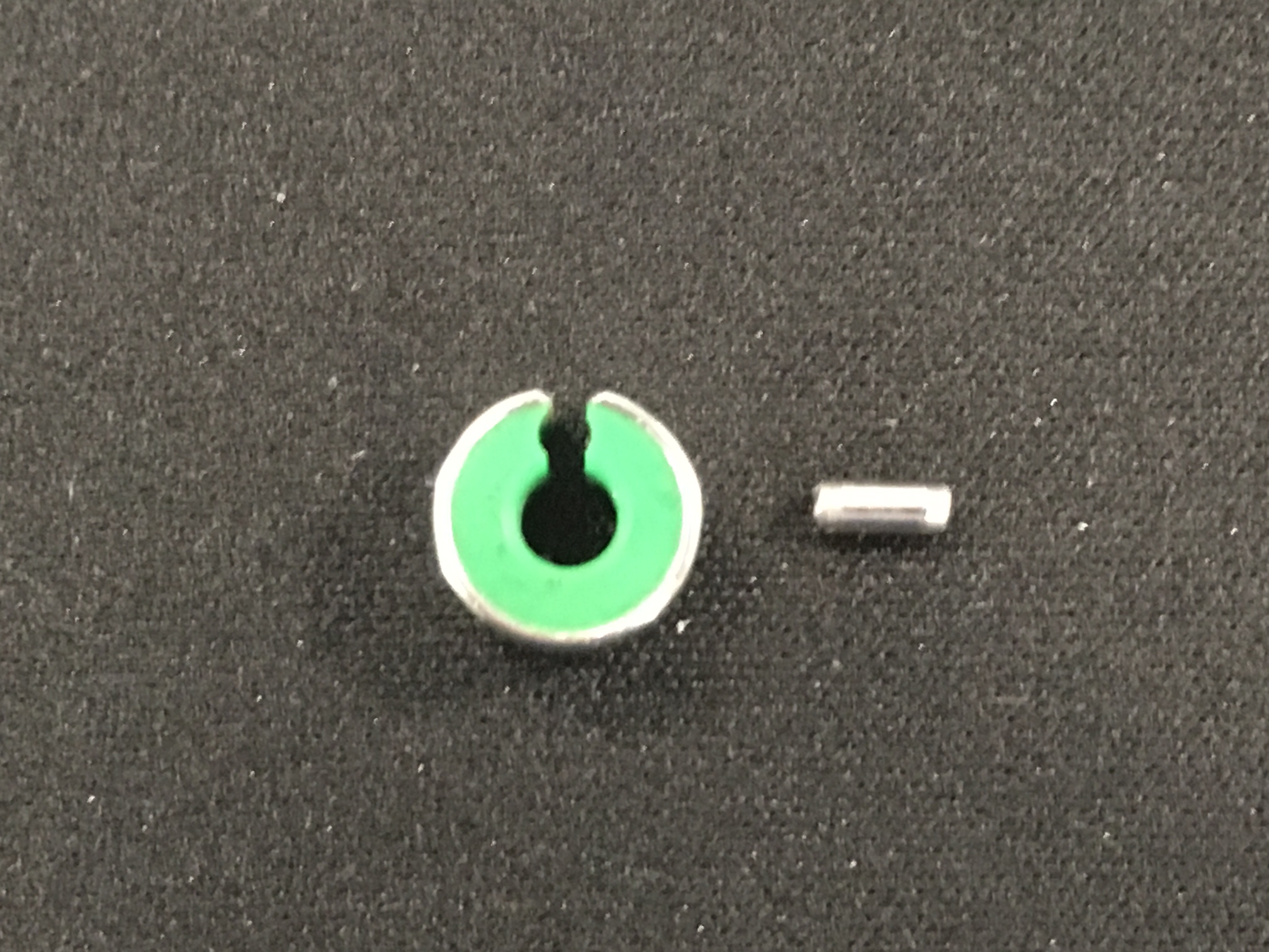 vets-now-john-williams-border-terrier-case-study-surgery2 A small metal pin lies next to a ring with a green interior and a slit, on a textured black surface.
