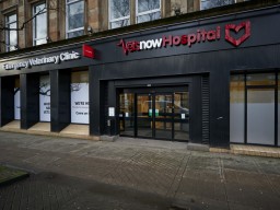 A veterinary hospital with glass doors in an urban setting; signs read Emergency Veterinary Clinic and Vets Now Hospital. Nearby windows display, WE'RE HERE WHEN YOU NEED US. VETS NOW. Come on in.