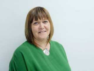 Laura Black of Vets Now A person with shoulder-length brown hair, wearing a green top and a silver pendant, is smiling against a plain white background.