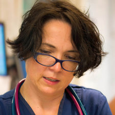 A person wearing glasses and a stethoscope reads attentively, focusing on something in front of them, within a professional or medical setting.