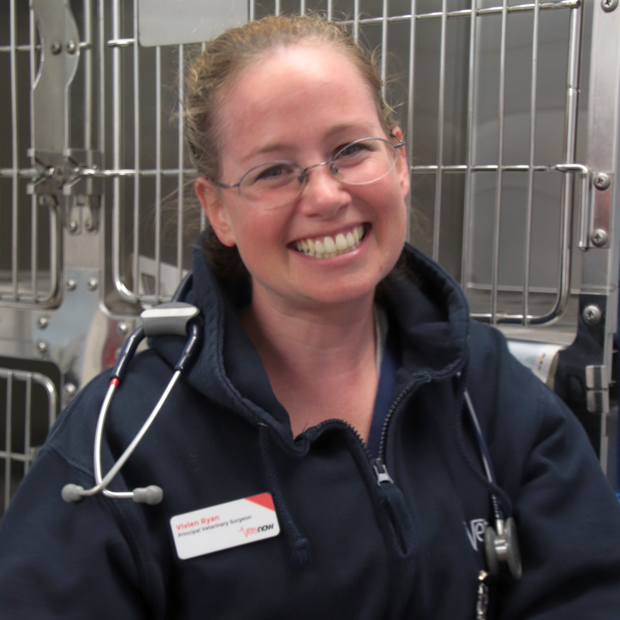 A woman with a stethoscope smiles in front of metal cages. Her name tag reads: 
