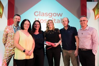 Vets Now Glasgow hospital receiving a MAD award Six people stand together smiling on stage, holding an award. Behind them, a sign reads