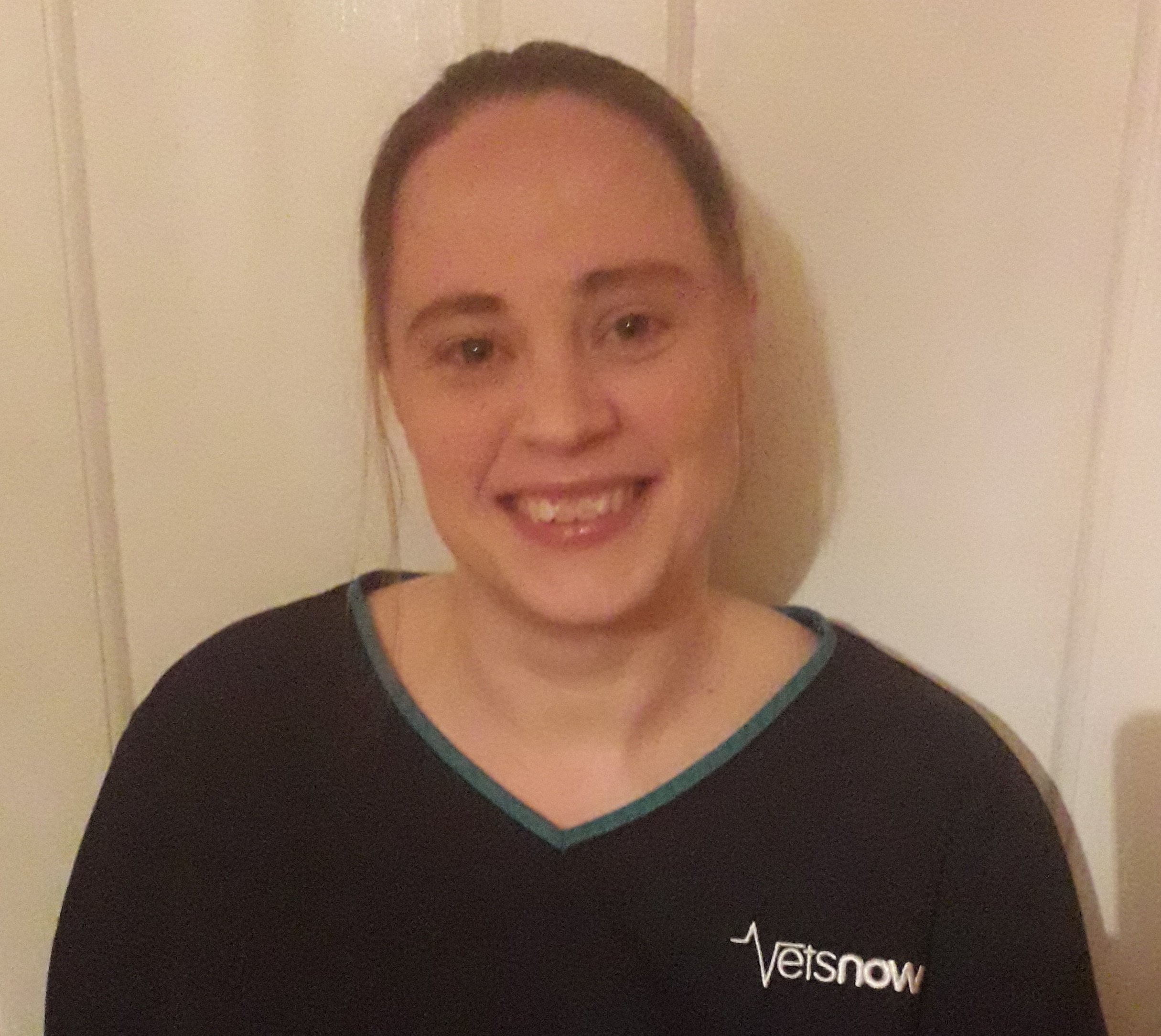 A person smiles while wearing a dark shirt with the logo 