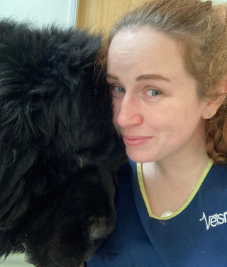 caitlin_donovan_1 A large black dog nuzzles against a woman smiling softly; she wears a navy shirt with partially visible text