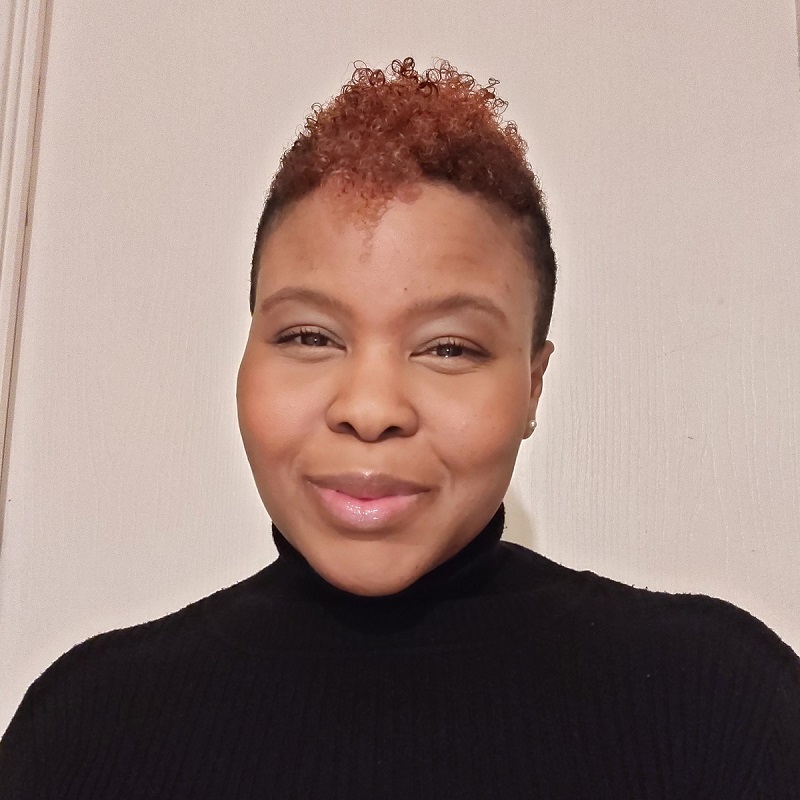 A person wearing a black turtleneck smiles softly, set against a plain, light-colored wall background.