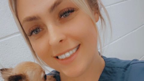 A close-up of veterinarian Emma Black in her Vets Now uniform, smiling as a small Chihuahua cuddles close to her shoulder.