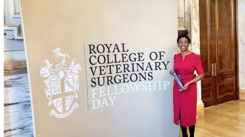 Mandisa Greene in a red dress holding an award stands next to a sign reading 