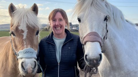 Fiona McLeod smiling while standing with horses in a field.
