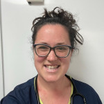 Anneka Phillips smiling in her veterinary uniform, wearing glasses and a stethoscope.