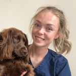 Harriet Robinson holding a brown spaniel and smiling, wearing navy scrubs.