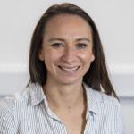Zara Kennedy smiling in a light striped blouse against a plain background.