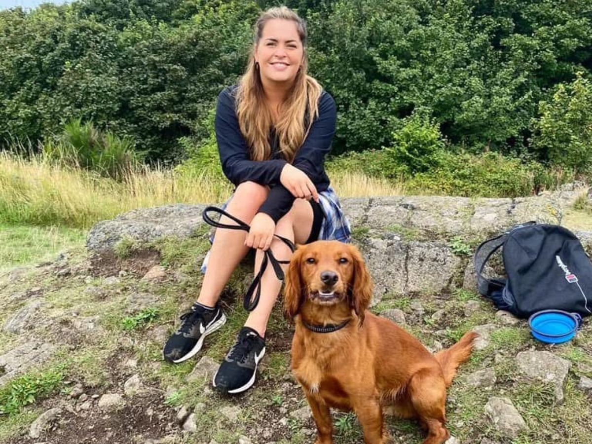 Megan_Hull An image of Megan Hull sitting on a rock with her dog during a countryside walk.